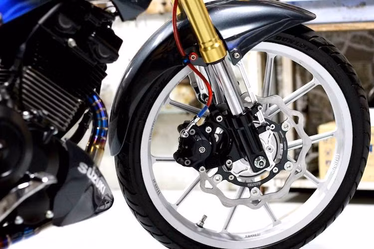 Vốn được trang bị phuộc ống lồng ở phía trước nhưng trên bản độ này, chiếc Satria đã được thay cặp phuộc USD thể thao và cứng cáp hơn. Bên cạnh phuộc, hệ thống phanh trước của chiếc xe cũng được nâng cấp triệt để với heo Brembo 2 pis đối xứng và đĩa hoa Galfer.