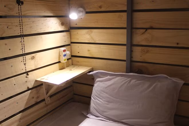 Trên giường còn có một chiếc kệ nhỏ, đèn chiếu sáng và ổ điện, đủ để khách sạc điện thoại và sử dụng laptop.