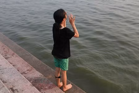 Một bé gái bị chảy máu chân vì nhảy, đùa nghịch dưới nước, đang đứng gọi các bạn vào bờ.