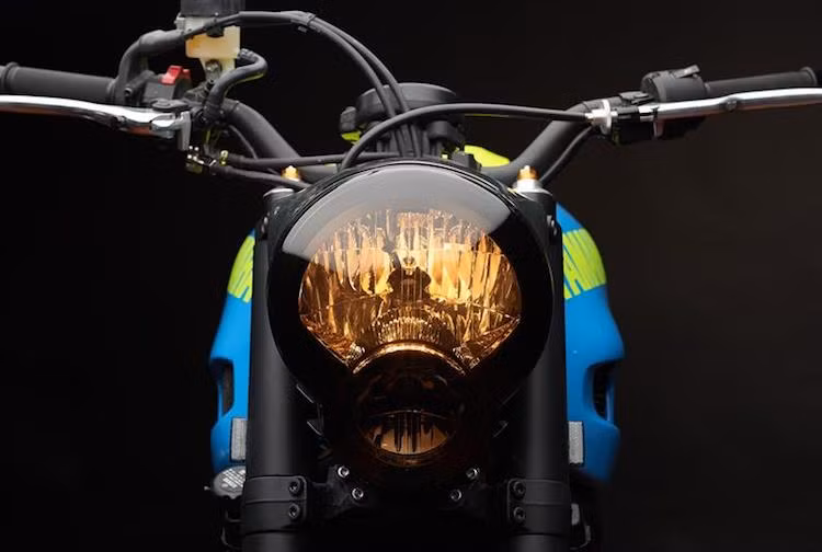 Nằm giữa cặp phuộc của R6 là một chi tiết lấy từ một chiếc Yamaha khác - đèn pha của MT-01 đời cũ với chóa sơn màu trà đậm. Ở ngay phía trên, ghi-đông nguyên bản của xe cũng đã được thay bằng tay lái từ Yamaha MT-09. Đặc biệt, đèn xi-nhan của chiếc xe đã được David tích hợp khéo léo vào tay phanh và tay côn.