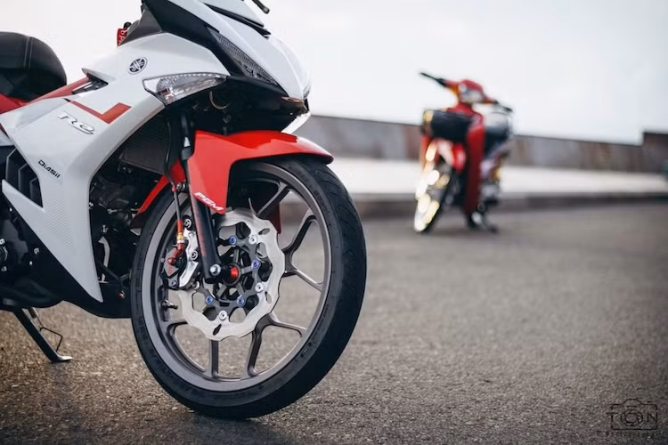 Cặp mâm nguyên bản của Exciter đã được chủ xe thay bằng mâm Racing Boy 5 cánh kép với thiết kế tương tự mâm nguyên bản trên Yamaha R3. Lốp trước có bản hẹp hơn xe nguyên bản, chỉ 70/80 thay vì 80/90. "Nhân tiện" nâng dàn chân, hệ thống phanh của chiếc xe đã được chủ xe nâng cấp với heo Frando 2 pis đối xứng kèm pát CNC và đĩa Galfer.