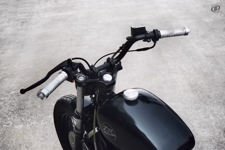 Ghi-động nguyên bản trên GN250 đã được DuongDoan thay bằng ghi-động cao hơn, đương nhiên cũng được sơn lại với màu đen mờ cực "lì". Nằm ở cuối ghi-đông là cặp bao tay nhôm CNC cùng xi-nhan gắn gù - những chi tiết đặc trưng của xưởng độ Hà Nội này.