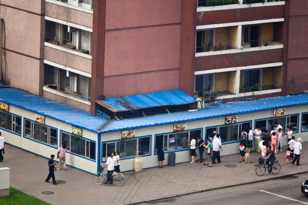 Dãy cửa hàng thực phẩm quốc doanh gần khách sạn Koryo ở thủ đô Bình Nhưỡng của CHDCND Triều Tiên. Các cửa hàng này bán khá nhiều món ăn, từ bánh bao, bánh bèo chige, kimchi Triều Tiên cho đến bánh pizza kiểu Italia. Ảnh: Hiroji Kubota/ Magnum Photos.