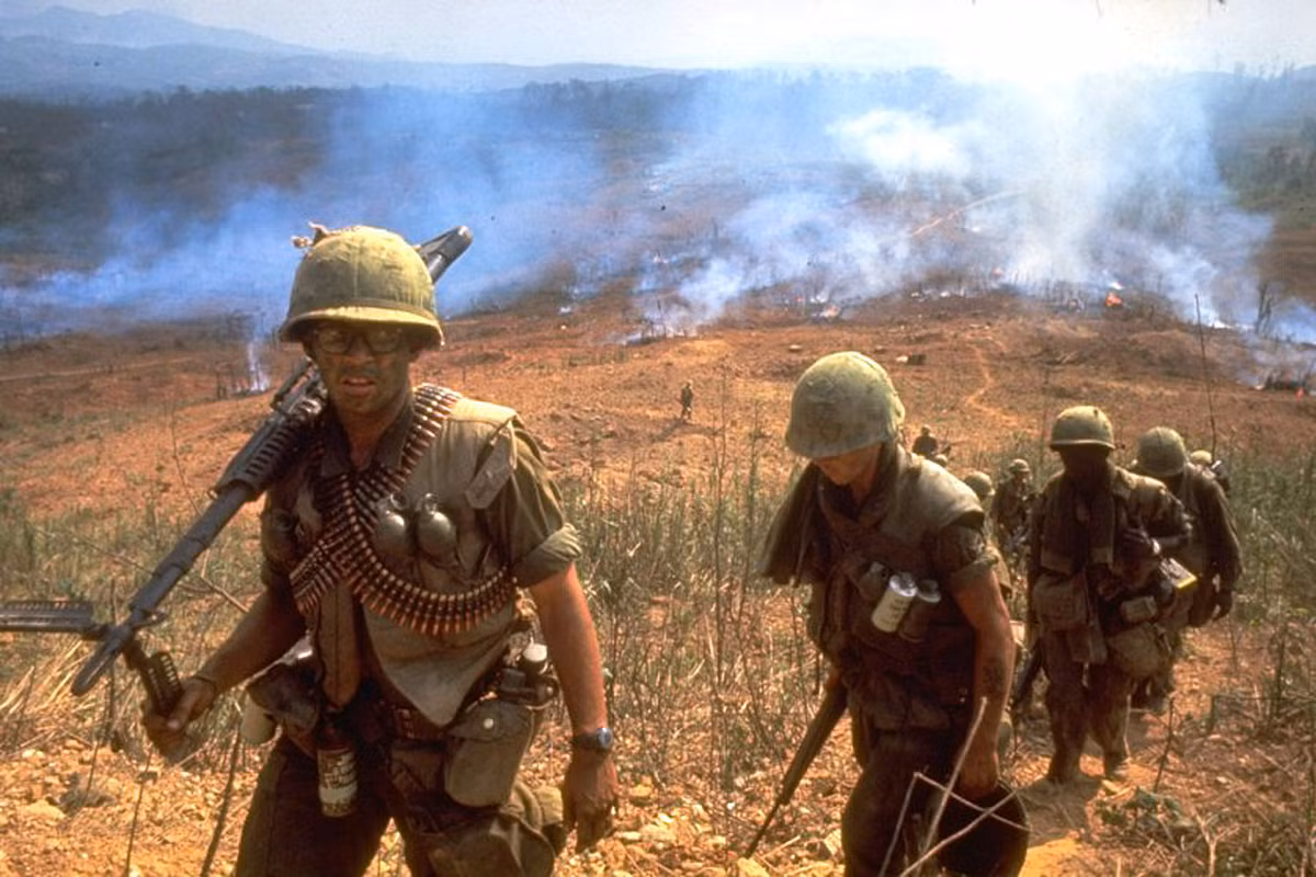 Lính Mỹ di chuyển trên một lối mòn, sau lưng là ngôi làng bị thiêu rụi. Ảnh: Larry Burrows.