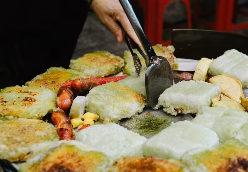  Bánh chưng rán thơm ngon: Những chiếc bánh chưng kích thước nhỏ bằng bàn tay người lớn, được xếp đều lên chiếc mâm nhôm tròn, bên dưới đặt bếp than hồng. Sau những tiếng xèo xèo là lớp ngoài nâu vàng, giòn tan, bên trong là lớp gạo nếp nóng hổi, hơi mềm xốp, cùng đậu xanh chín nhuyễn và vài miếng thịt mỡ béo ngậy. Ảnh minh họa