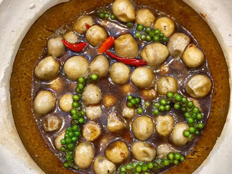  Nấm rơm kho tiêu xanh: Nấm rơm gọt rửa, ngâm nước muối pha loãng, rồi rửa lại cho sạch sẽ, để ráo. Làm nóng chảo hoặc nồi. Cho dầu ăn, boa rô 1/2 muỗng cafe tiêu xanh giã dập vào phi cho dậy mùi thơm thì tắt bếp. Cho nấm, xì dầu, đường, ớt bột vào trộn đều để 15 phút cho thấm gia vị một chút. Bật lửa lên lại, nấu sôi cho mấy chùm tiêu xanh vào.