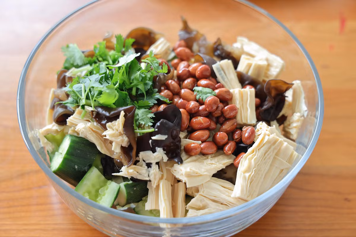 Bước 6: Cho nấm mộc nhĩ, mì váng đậu đã ráo nước và dưa chuột vào chung một bát, sau đó đổ lạc vừa chiên và rau mùi vào.