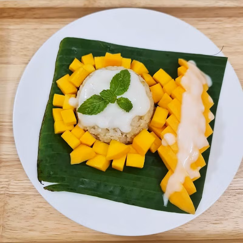 Ở Thái Lan, mùa hè thường rất nóng bức và oi ả, vì vậy xôi xoài chính là món ăn lý tưởng để làm dịu đi cái nóng. Với sự tươi mát của xoài cùng độ dẻo và béo ngậy của xôi, món tráng miệng này như một thức quà hoàn hảo để giải nhiệt trong những ngày hè oi ả. Mỗi miếng xôi xoài mang đến cảm giác mát lạnh, nhẹ nhàng và đầy đủ dưỡng chất, giúp bạn cảm thấy tươi mới và sảng khoái. Ảnh Holivn Travel