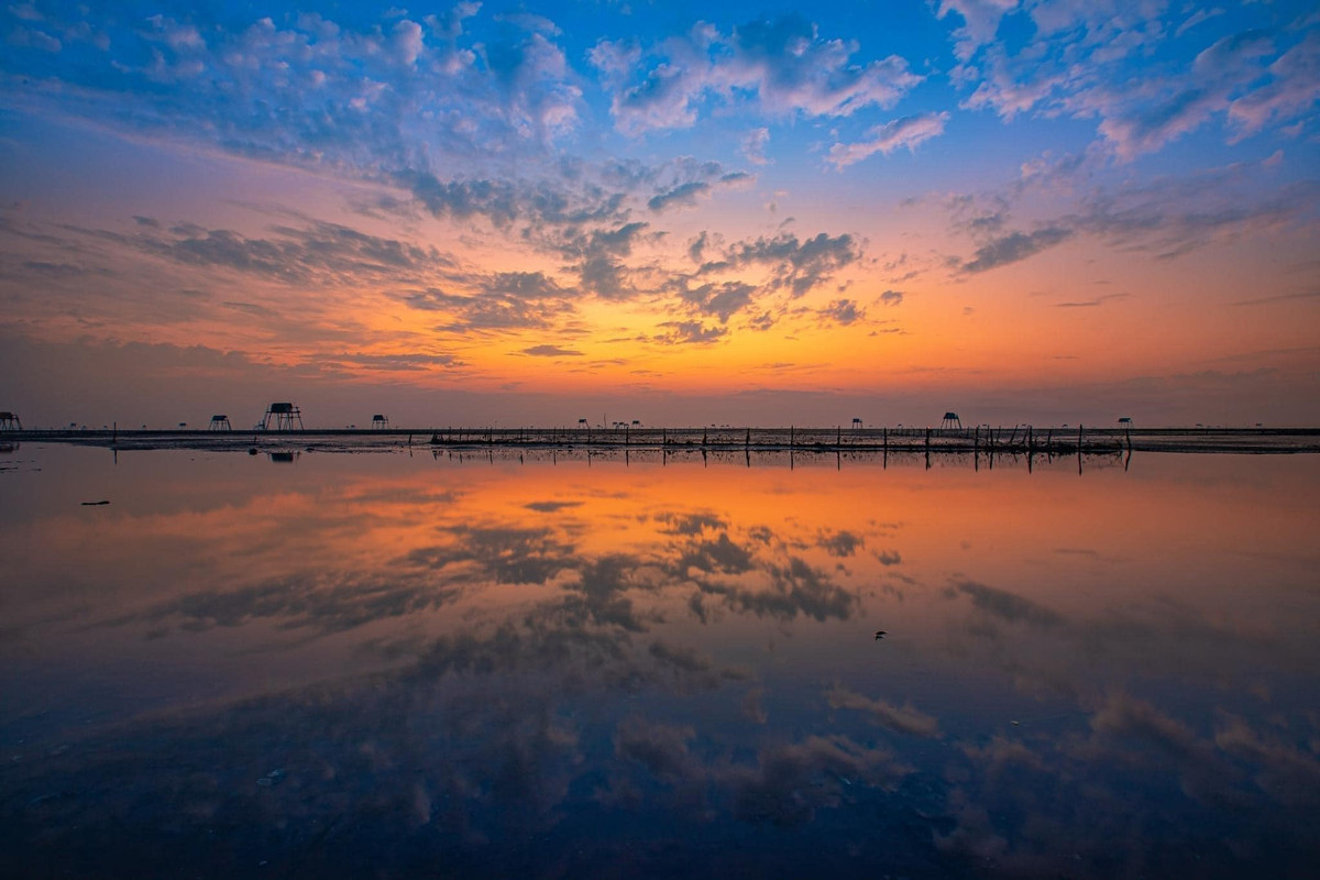 Từng đợt sóng lăn tăn lấp lánh ánh sáng, hàng chòi canh ngao hiện lên trong sương sớm tạo nên một khung cảnh vừa hư vừa thực.