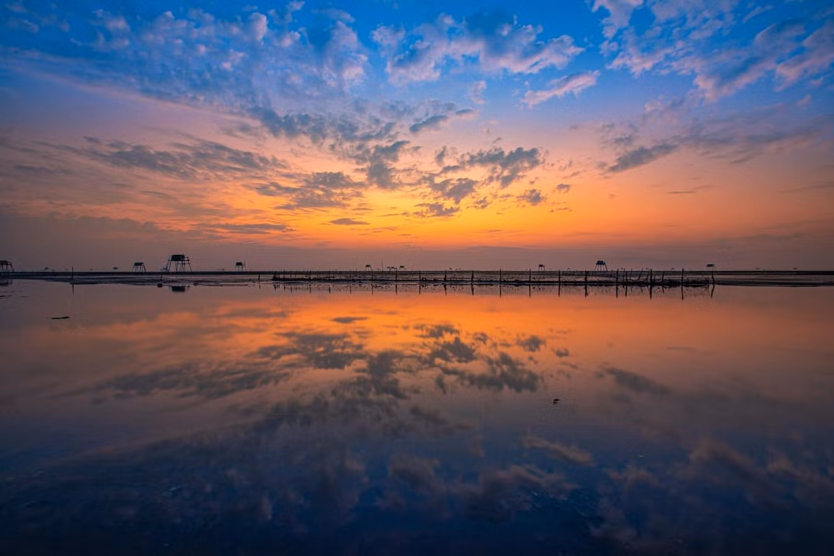 Từng đợt sóng lăn tăn lấp lánh ánh sáng, hàng chòi canh ngao hiện lên trong sương sớm tạo nên một khung cảnh vừa hư vừa thực.