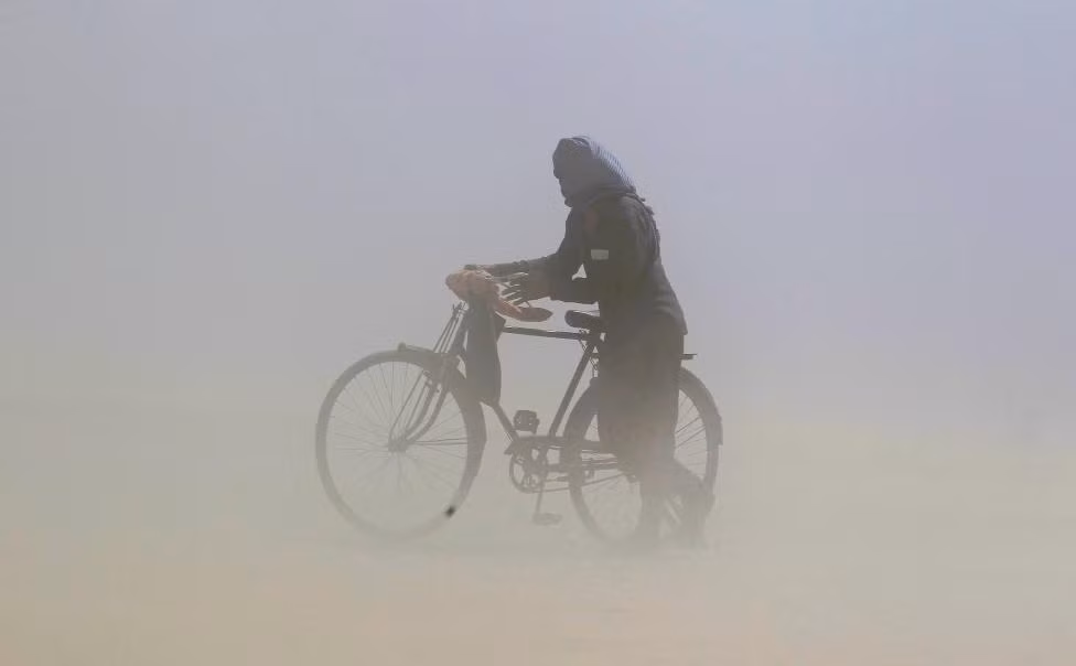 Người đàn ông che kín mặt khi dắt xe đi dưới trận bão cát trên bờ sông Ganga ở Allahabad ngày 12/4/2016.