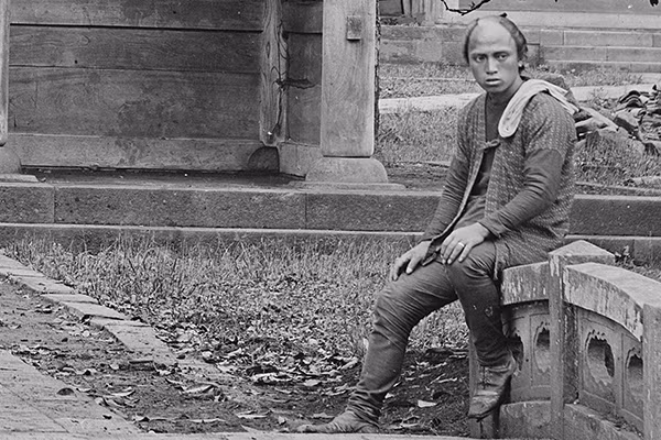 Cận cảnh người đàn ông Nhật Bản ngồi trước chùa Sengakuji có đeo một chiếc nhẫn và đi ủng kiểu phương Tây.