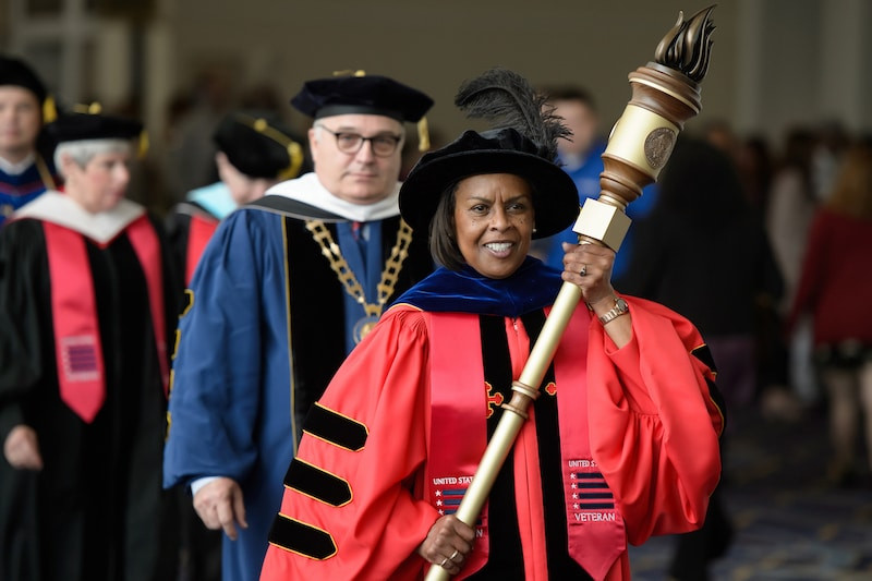 Theo trang Dreamstime, tất cả lễ tốt nghiệp đại học tại Mỹ đều có nghi thức mở đầu bằng việc giáo sư hoặc người đứng đầu nhà trường (tức hiệu trưởng) tiến vào bà cầm trên tay quyền trượng của trường.