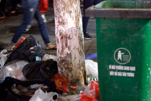 Rác bị vứt đống đầy gốc cây trong khi thùng rác nằm ngay cạnh nhưng không ai bỏ vào.