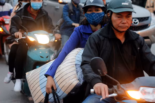 Tay xách, nách mang dù đang ngồi trên xe máy.