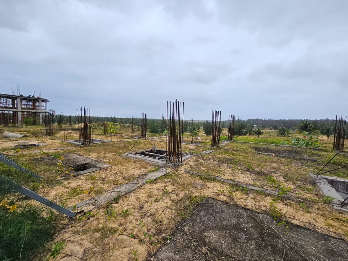 Sau nhiều năm triển khai, bên cạnh dãy nhà được xây thô là hàng loạt trụ sắt nằm chỏng chơ trên bãi đất trống.