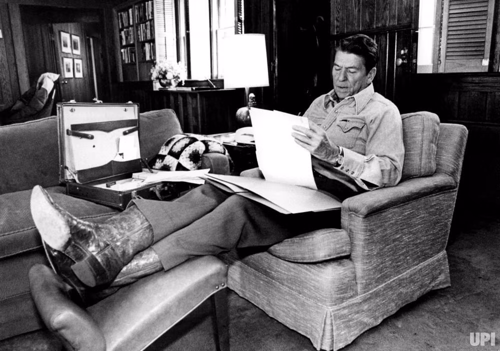 Còn Tổng thống Ronald Reagan ngồi gác chân lên ghế trong lúc đọc giấy tờ tại Trại nghỉ dưỡng David.