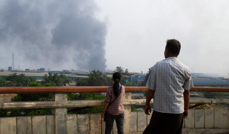 Người dân đứng nhìn khói đen bốc lên từ đám cháy tại một nhà máy khi lực lượng an ninh trấn áp những người biểu tình phản đối chính quyền quân sự ở Hlaingthaya, Yangon, hôm 14/3.