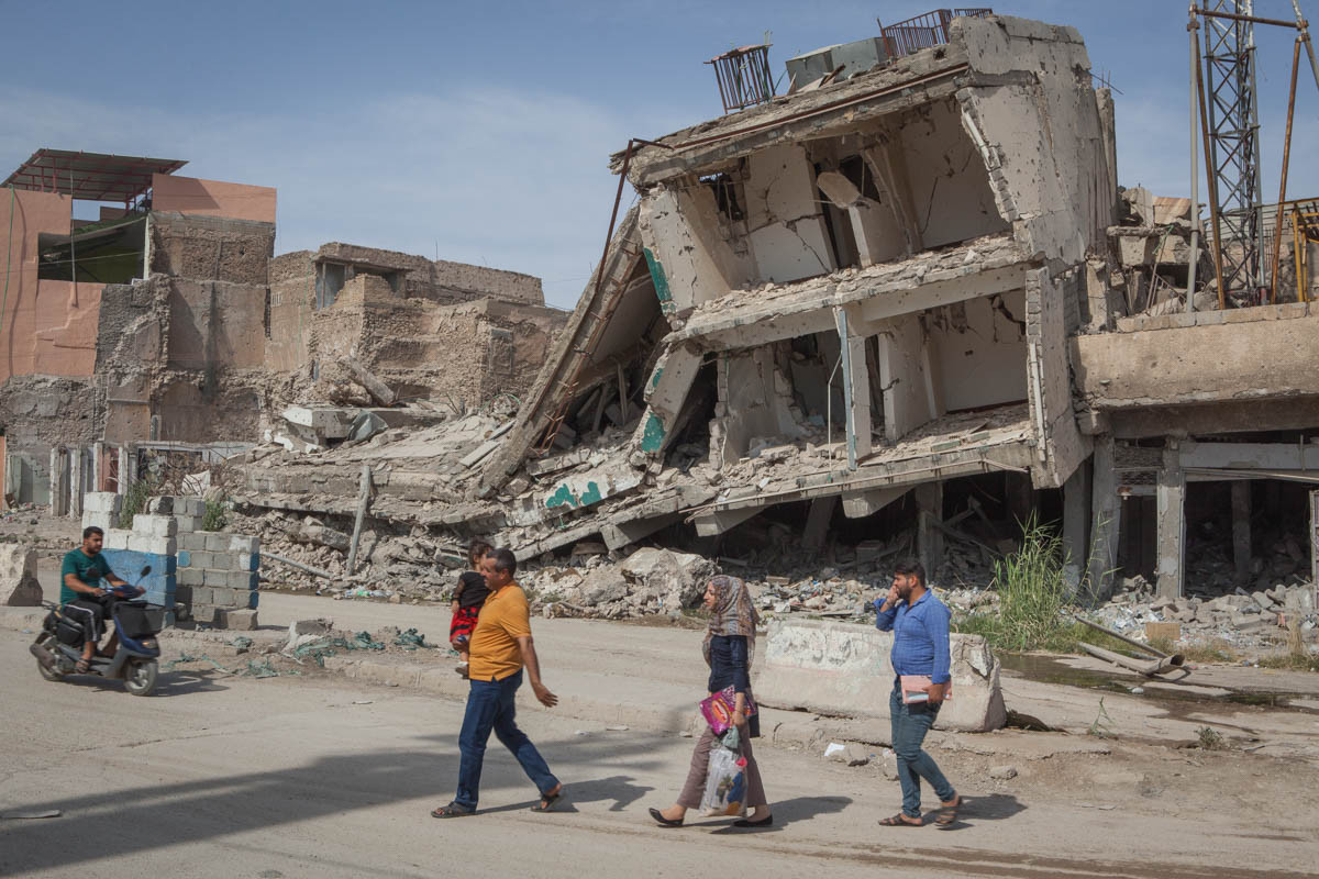 Người dân đi qua những ngôi nhà đổ nát ở Mosul.