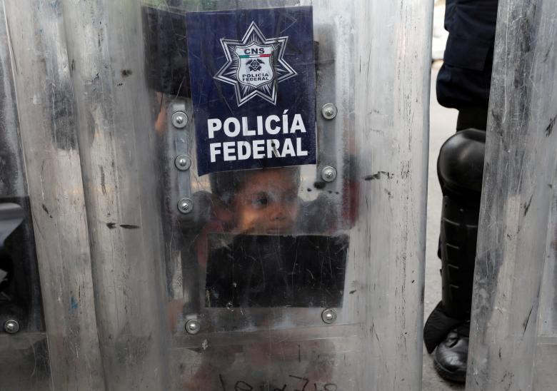 Một bé trai nhìn qua tấm khiên của cảnh sát chống bạo động Mexico ngày 22/11.