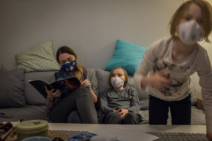 Eva Ciesielska đọc sách cho các con của mình Zoe (giữa) 9 tuổi và Lena 6 tuổi. Họ phải đeo khẩu trang kể cả khi ở trong nhà. Ô nhiễm không khí ở Krakow khiến nhiều người mắc các bệnh về đường hô hấp, sinh non và chết sớm, làm chậm sự phát triển nhận thức ở trẻ em.