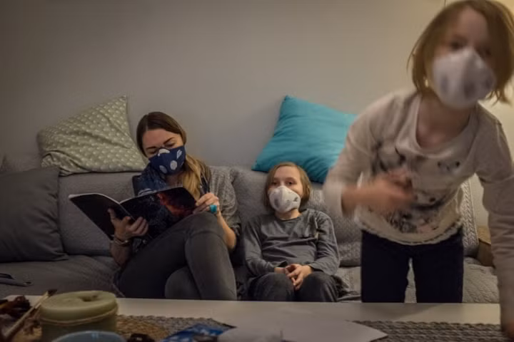 Eva Ciesielska đọc sách cho các con của mình Zoe (giữa) 9 tuổi và Lena 6 tuổi. Họ phải đeo khẩu trang kể cả khi ở trong nhà. Ô nhiễm không khí ở Krakow khiến nhiều người mắc các bệnh về đường hô hấp, sinh non và chết sớm, làm chậm sự phát triển nhận thức ở trẻ em.