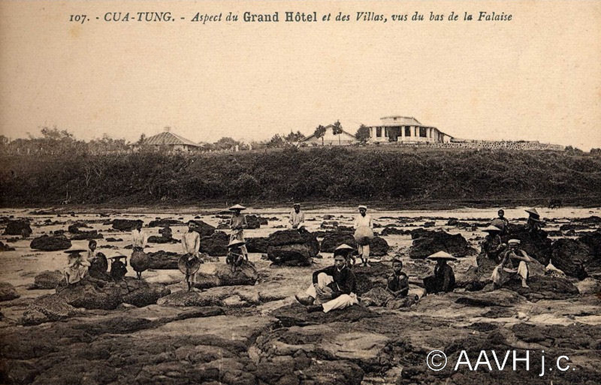 Người lao động bản xứ ngồi nghỉ ở bãi đá trên bờ biển Cửa Tùng, 1930. Phía xa là khách sạn Grand. Ảnh: Aavh.org.
