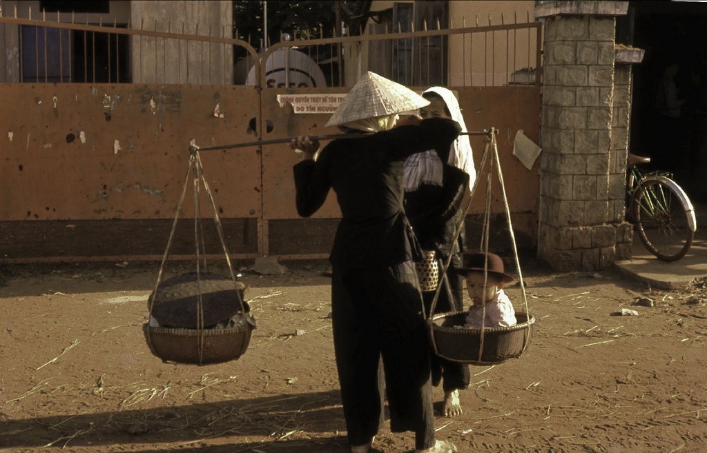 Một bà mẹ gánh con nhỏ bằng đòn gánh khi mưu sinh trên đường phố. Ảnh: Culturalspot.org.