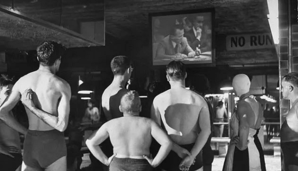 Những người đi bơi tại một bể bơi công cộng chăm chú theo dõi một bản tin thời sự năm 1950.