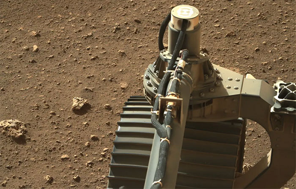 Hình ảnh bánh xe trước bên trái của Perseverance, xung quanh là những viên đá loang lổ nằm rải rác.