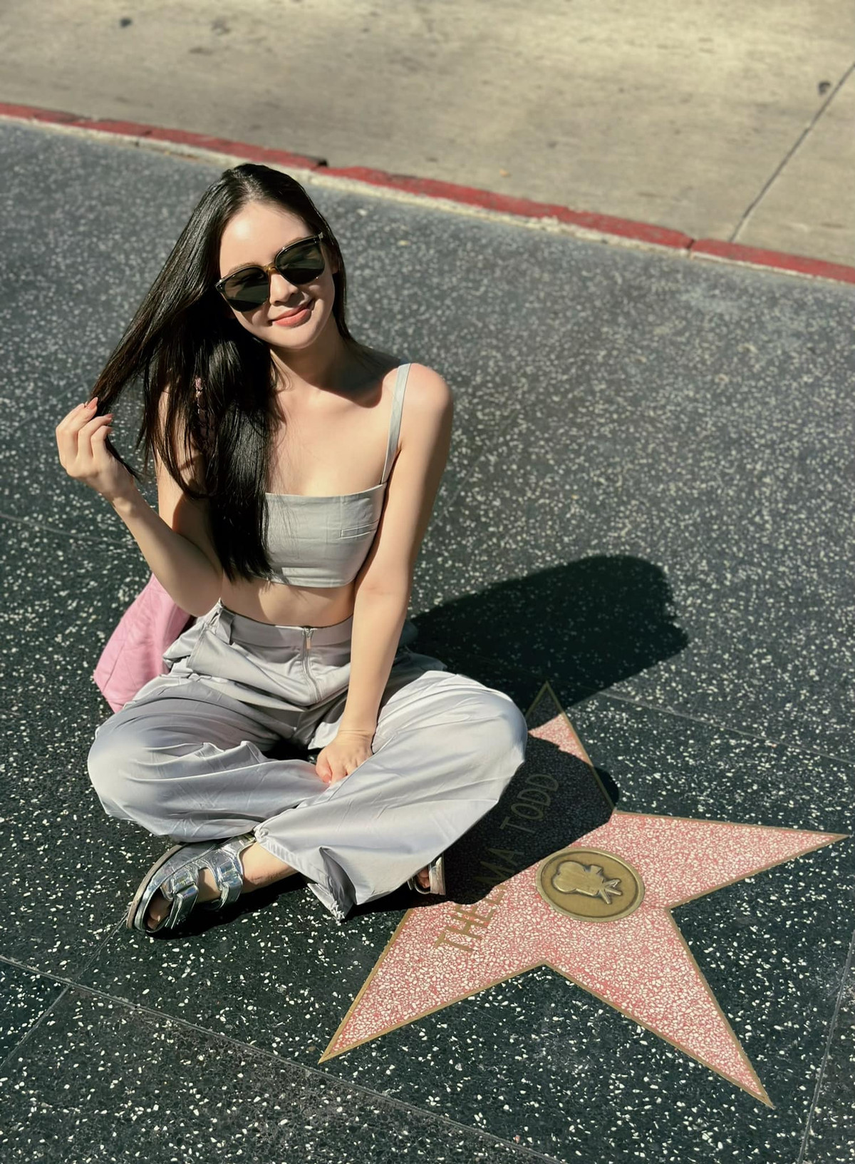 Trong hình, người đẹp diện áo hai dây dáng croptop cùng quần cargo, phối thêm 1 đôi sandals cùng màu, ngồi tạo dáng ở Đại lộ Danh vọng Hollywood.
