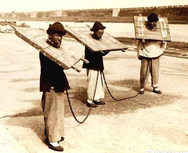 Ba tù nhân đeo cùm gỗ và trói bằng dây xích trong lúc di chuyển tới nhà tù.