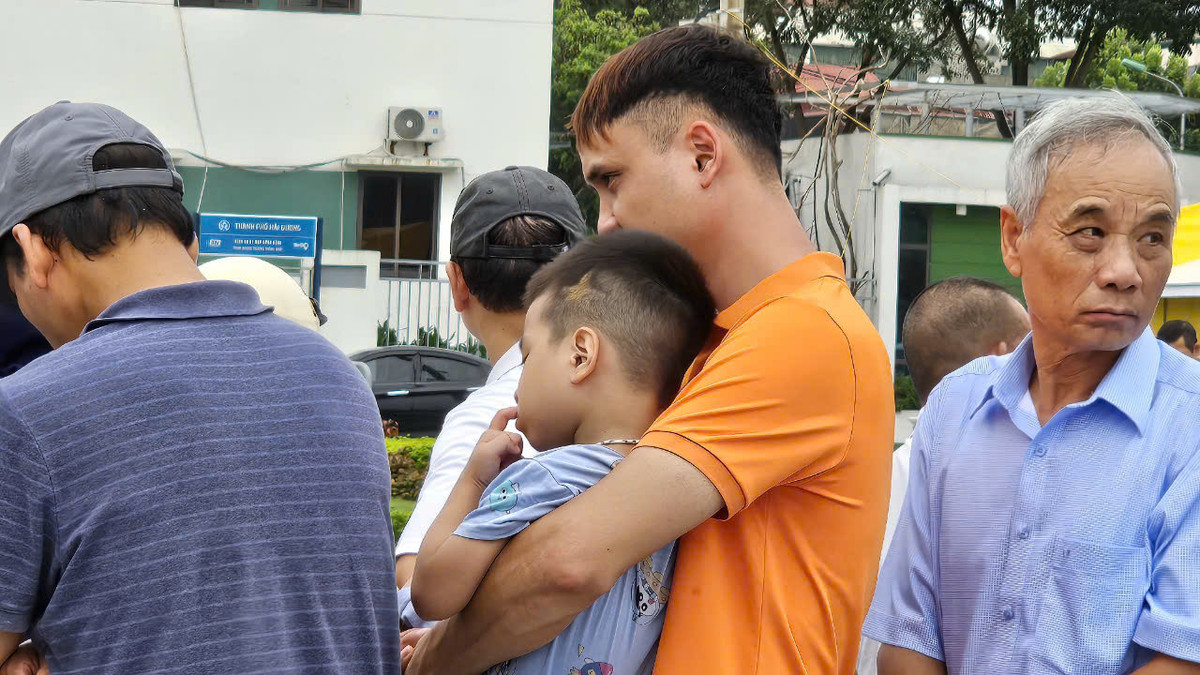 Một người đàn ông bế con nhỏ đi xếp hàng mua cá.