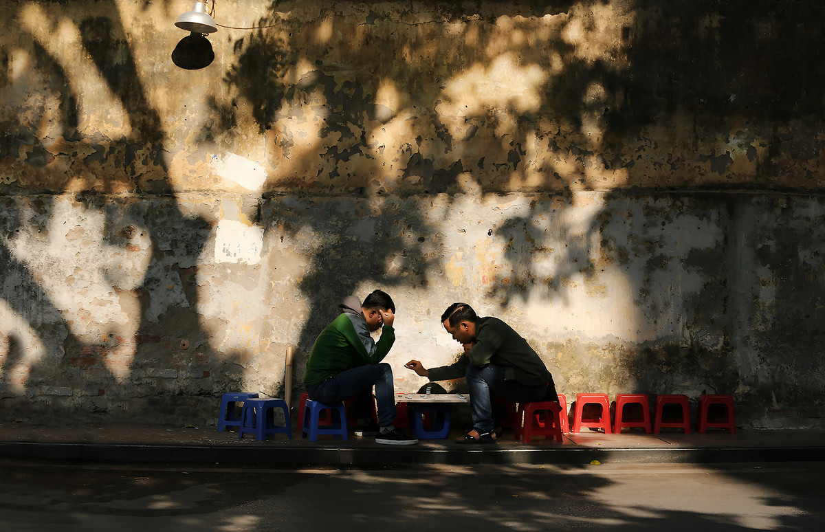 Tại các ngõ ngách ở nhiều con phố cổ, người ta dễ dàng bắt gặp hình ảnh những bậc trung niên và người cao tuổi ngồi uống trà đá hoặc chơi cờ. Khoảnh khắc đó đậm nét Hà Nội hơn khi xung quanh họ là những ô cửa ngôi nhà cổ cùng các vệt ánh sáng nhạt chiếu xuống những mảng tường rêu phong, bong tróc. Ảnh: Vũ Minh Quân.