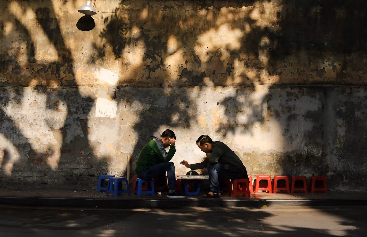 Tại các ngõ ngách ở nhiều con phố cổ, người ta dễ dàng bắt gặp hình ảnh những bậc trung niên và người cao tuổi ngồi uống trà đá hoặc chơi cờ. Khoảnh khắc đó đậm nét Hà Nội hơn khi xung quanh họ là những ô cửa ngôi nhà cổ cùng các vệt ánh sáng nhạt chiếu xuống những mảng tường rêu phong, bong tróc. Ảnh: Vũ Minh Quân.