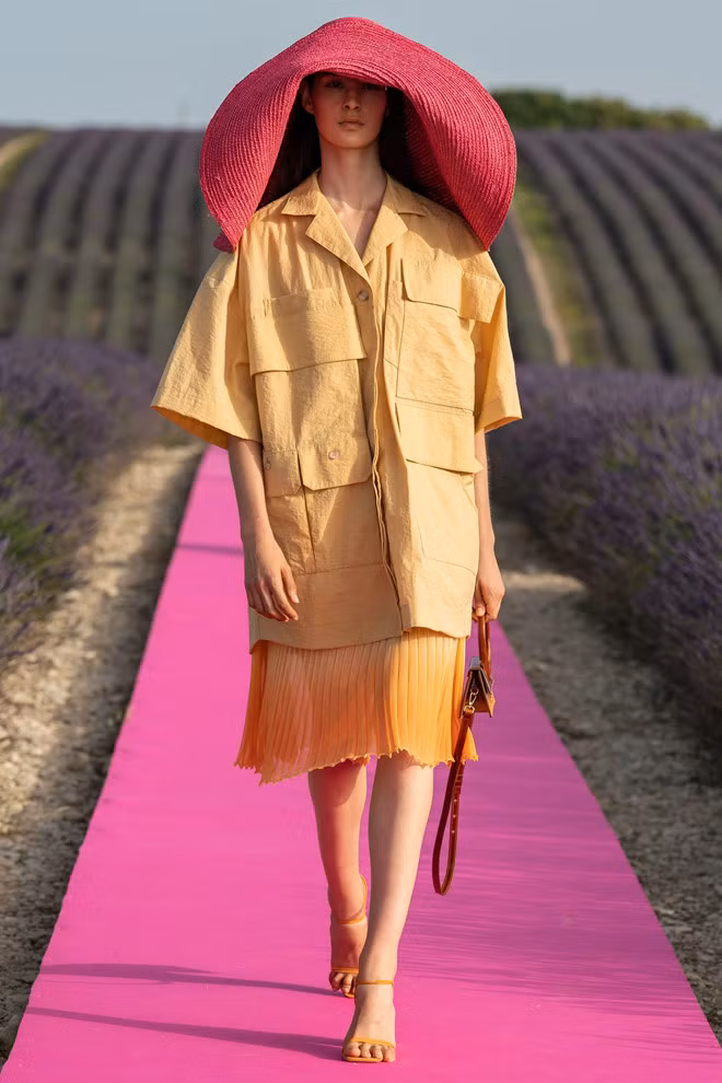 Jacquemus biến tấu thêm nhiều màu sắc cho chiếc mũ cói quá khổ thịnh hành từ năm 2018. Người mẫu diện phụ kiện mùa hè kết hợp áo sơ mi phom dáng oversized, chân váy tulle nữ tính.