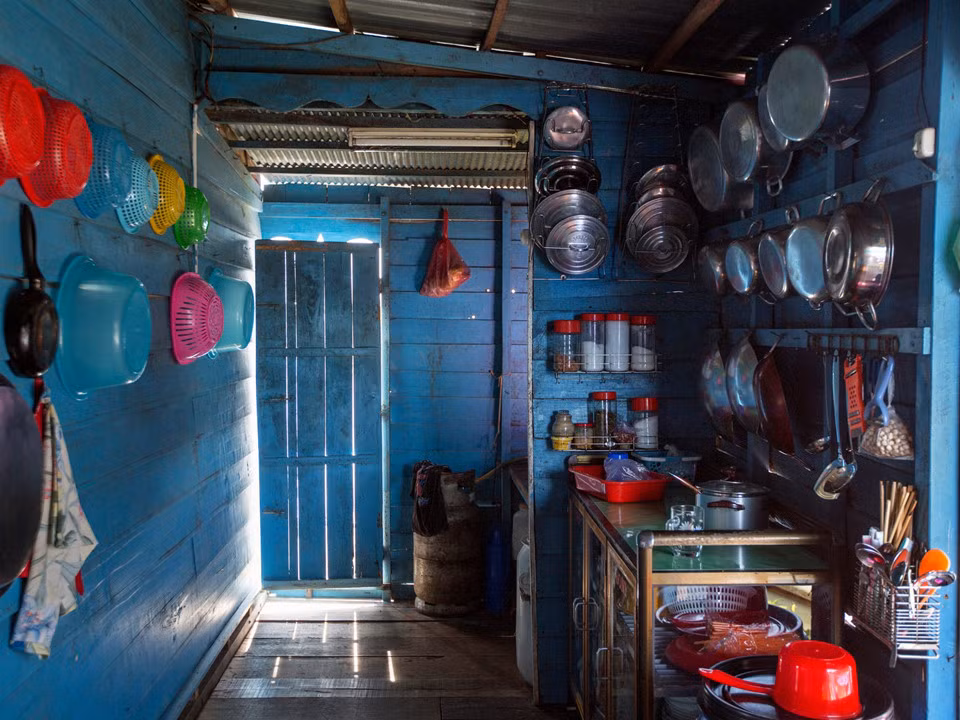 Đây là một gian bếp, trông rất bình thường trừ việc nó nằm trên mặt nước, chính xác là nằm trên Biển Hồ, Campuchia. Như mọi căn nhà khác ở đây, nó đối mặt với hàng loạt nguy cơ mà dòng nước mang lại, đặc biệt trong mùa mưa. Vào cuối tháng 7, lúc nào cũng có việc cho Taing Hoarith làm với ngôi nhà của ông. Khi thì ông phải sửa lại bức tường lợp bằng lá cọ đã bị bão làm hư, khi thì ông phải dọn dẹp đám cây mọc trong nước. Đôi khi ông phải lặn xuống bên dưới căn nhà, miệng ngậm một ống cao su và chèn vào những hũ xi măng đang giữ căn nhà đứng vững trên nước. Ảnh: New York Times