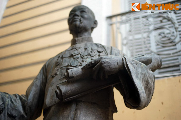 Hình ảnh ông Quách Đàm được thể hiện với tay trái cầm các cuộn văn bản ghi lại những khoản tài trợ mà ông dành cho vùng Chợ Lớn.