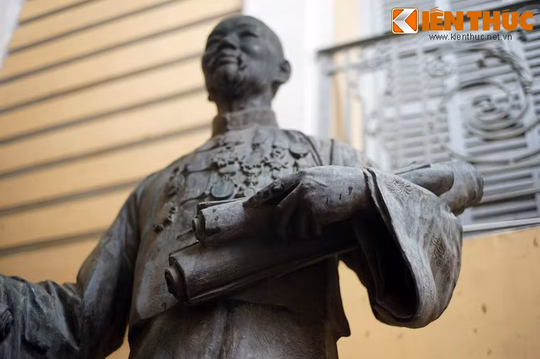 Hình ảnh ông Quách Đàm được thể hiện với tay trái cầm các cuộn văn bản ghi lại những khoản tài trợ mà ông dành cho vùng Chợ Lớn.