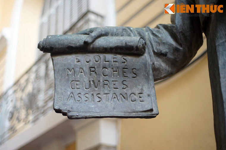 Tay phải của ông cầm một cuộn giấy ghi các chữ Pháp "Écoles, marchés, oeuvres, assistance", nghĩa là "Trường học, thị trường, việc làm, hỗ trợ", khái quát các cống hiến của ông cho xã hội.
