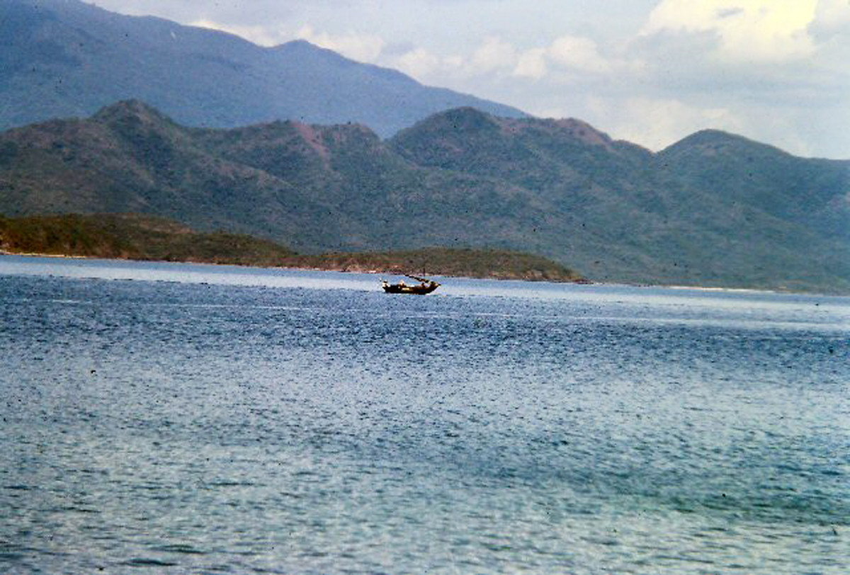 Một con thuyền với buồm được cuốn lại giữa khung cảnh kỳ vĩ của biển và núi. Ảnh: 459thsignal.org.