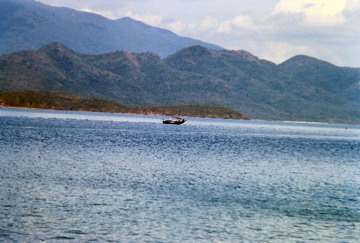 Một con thuyền với buồm được cuốn lại giữa khung cảnh kỳ vĩ của biển và núi. Ảnh: 459thsignal.org.