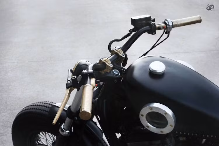 Tay lái nguyên bản của Harley 883 được giữ lại, nhưng bắt vào chảng 3 bởi cặp gù bằng đồng CNC. Ở hai bên đầu tay lái, những tay nắm và tay côn/phanh bằng đồng cũng đã thay cho tay "zin", trong khi cụm công tắc được tối giản một cách tối đa.