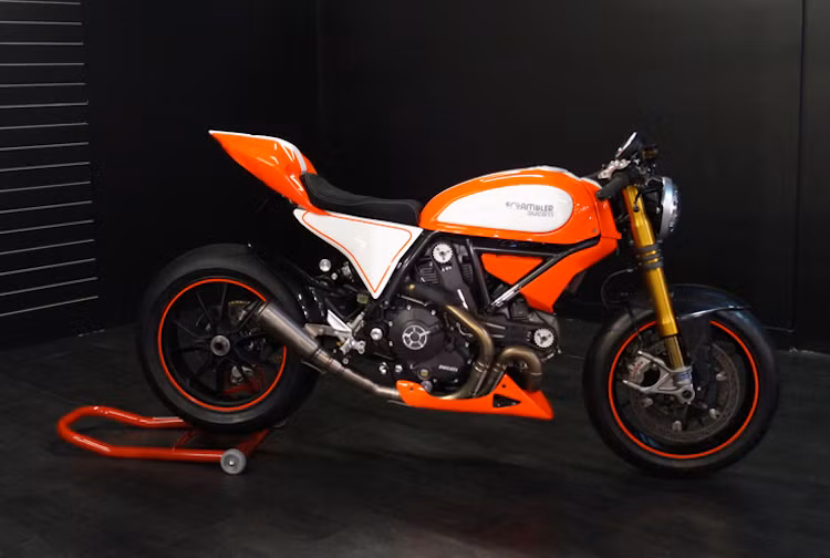 Bộ "mỏ cày" bên dưới động cơ cũng đã được Canberra Motorcycle Center chế riêng để khiến Scramblegale gợi nhớ nhiều hơn tới Panigale. Khối động cơ 803cc làm mát bằng gió nguyên bản của Scrambler không có thay đổi gì ngoài cổ pô độ kèm lon Arrow.