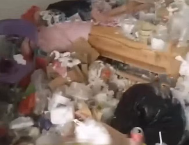 Mặc dù rác thải ngập ngụa khắp phòng nhưng cô gái đó vẫn ngồi ung dung trên giường như chưa hề có chuyện gì xảy ra. Mãi cho đến khi phát hiện bị quay clip, cô gái mới né mặt đi vì xấu hổ. Ảnh: Tổng hợp