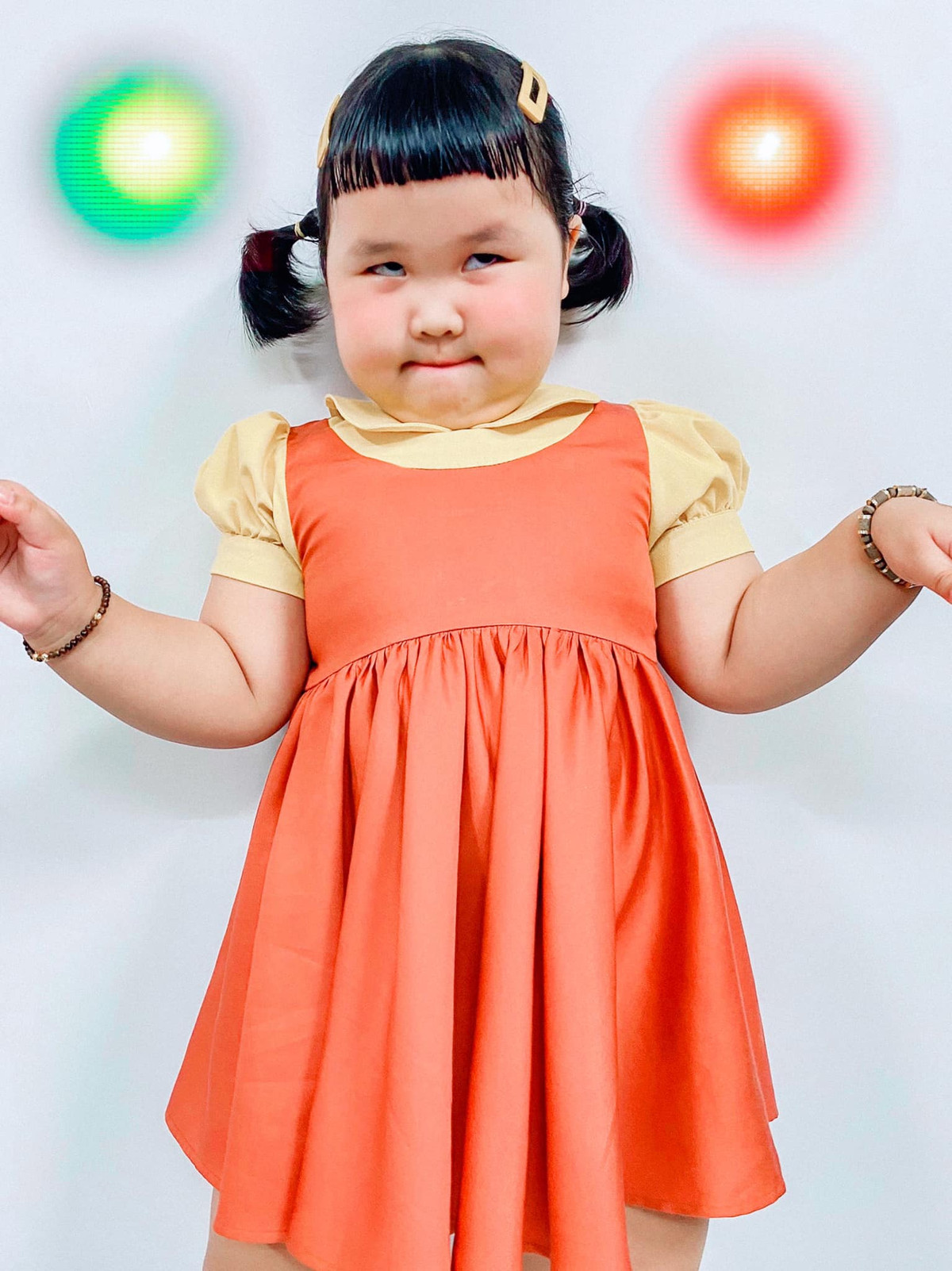 Cô bé khoác trên mình bộ váy màu cam cùng đôi giày đen và hai bím tóc xinh xắn y hệt như phiên bản gốc.