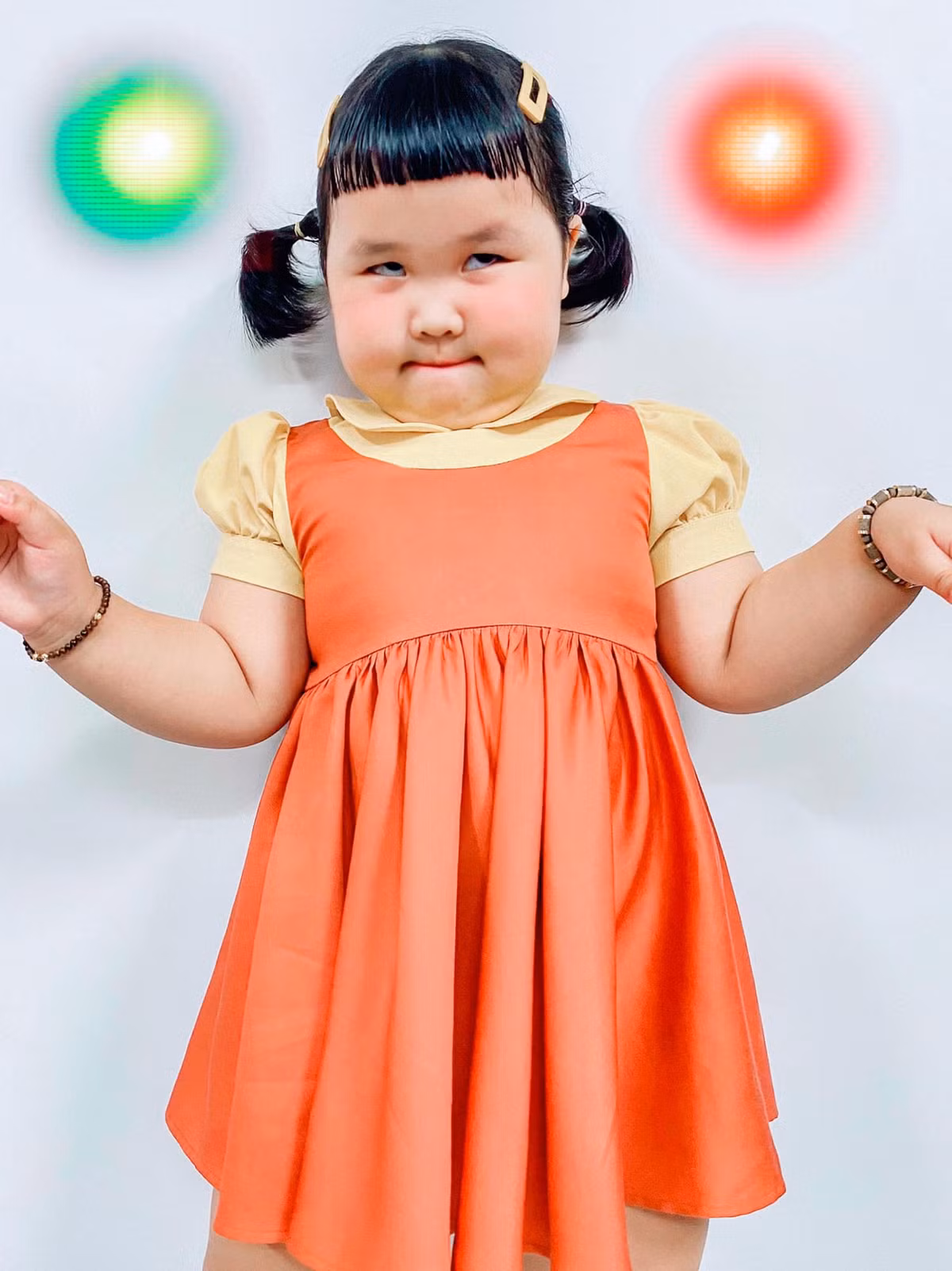 Cô bé khoác trên mình bộ váy màu cam cùng đôi giày đen và hai bím tóc xinh xắn y hệt như phiên bản gốc.