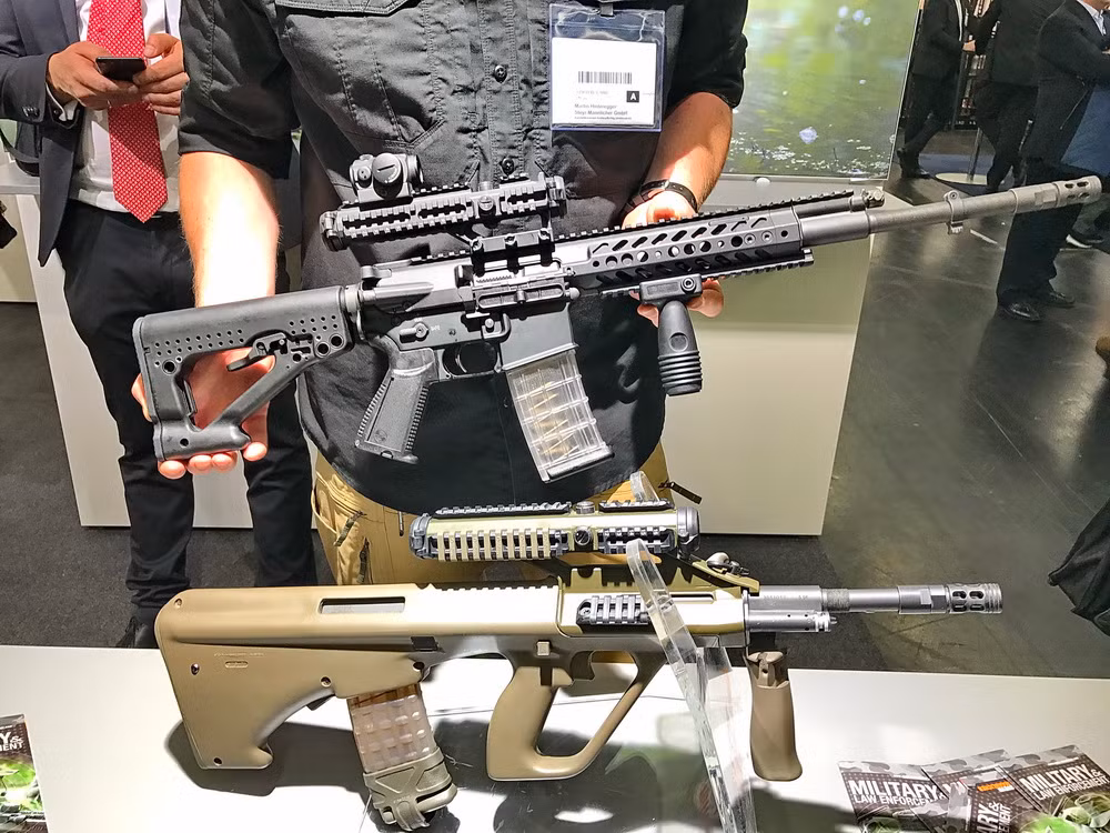 Với cỡ nòng 40,6 cm, khẩu Steyr RS556 sẽ có trọng lượng khoảng 4,2 kg (trọng lượng rỗng không mang đạn). Hộp tiếp đạn tiêu chuẩn của Steyr RS556 có thiết kế bằng nhựa trong suốt, dự trữ đạn 30 viên. Ảnh: Khẩu Steyr RS556 ở phía trên và khẩu AUG ở phía dưới. Nguồn ảnh: Firearm.