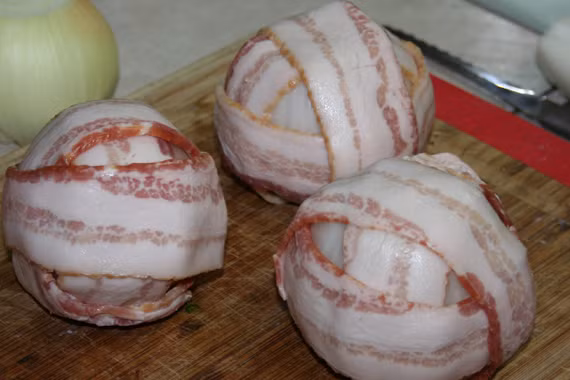 Bọc vỏ hành tây ngoài quả bóng thịt rồi quấn dải thịt xông khói bên ngoài. Sau đó, sử dụng tăm để cố định quả bom thịt trong quá trình nướng. Ảnh: BDT.