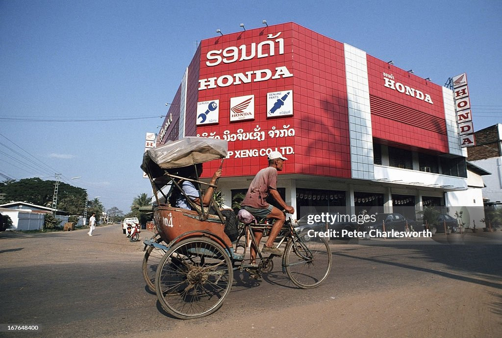 Người đạp xích lô chở khách đi ngang qua đại lý duy nhất của hãng xe máy Honda ở Vientiane.